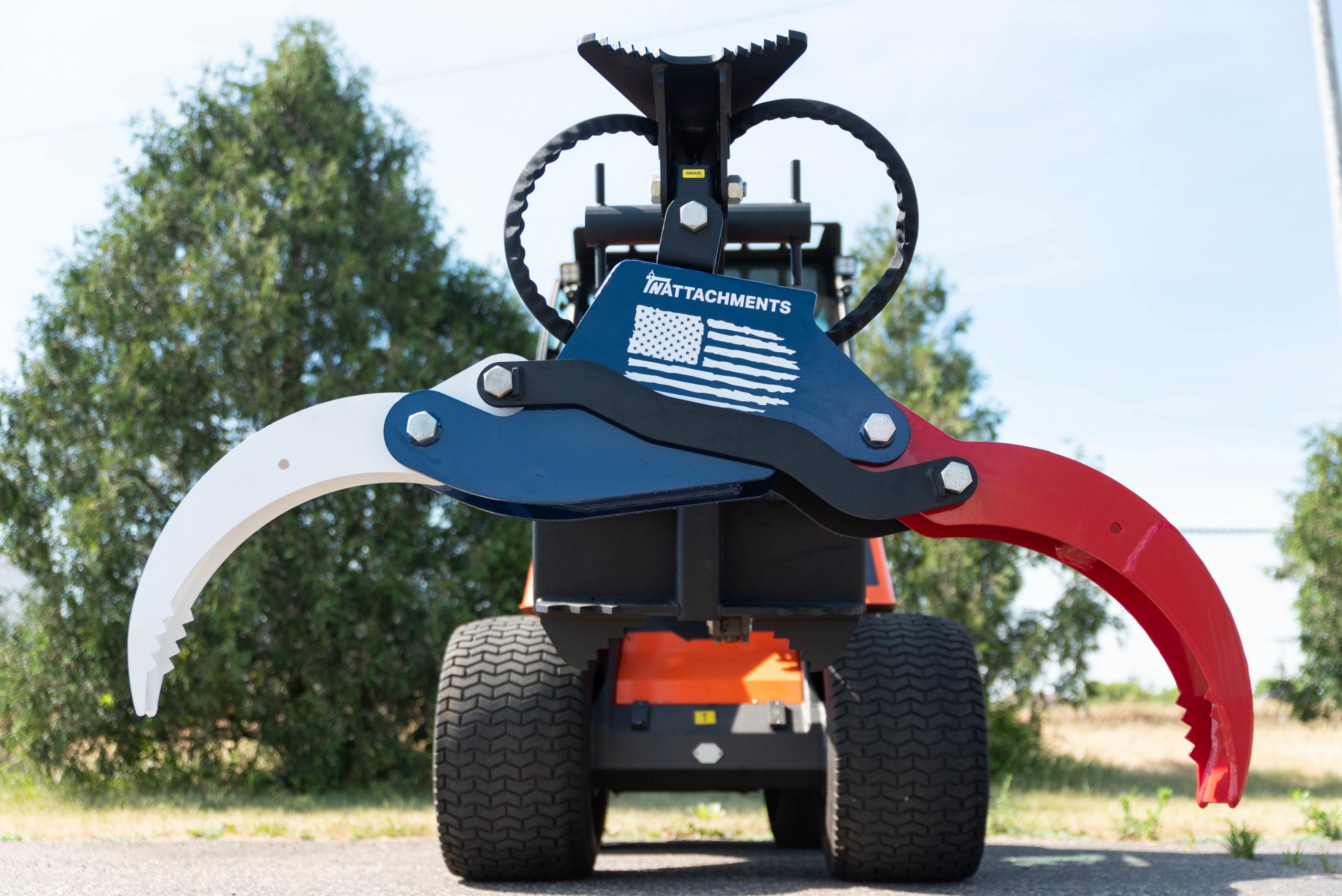 TNAttachments-HDMG-Mini-Grapple-at-TNE-Distributing TNAttachments HD Mini Grapple at TNE Distributing. Red, White and Blue Grapple3 Ton Power Rotation 61" Grapple Opening Internal Hose Routing High Strength 3/8" Steel Body, Transfer & Grapple Arms (AR400) 2.5" Hydraulic Cylinder Integrated Whale Tail Tree Pusher Angled Hanger With Fully Welded Side Gussets Large Integrated Rope Bollard Available in Universal Mini, MT, FSS & HD-Euro (Avant, MultiOne) Attachment Plates Optional Receiver Hitch & 1 Piece Milled Saw Scabbards. Custom Color Options To Match Your Loader
